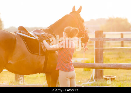 Woman preparing saddle for horseback riding in rural pasture