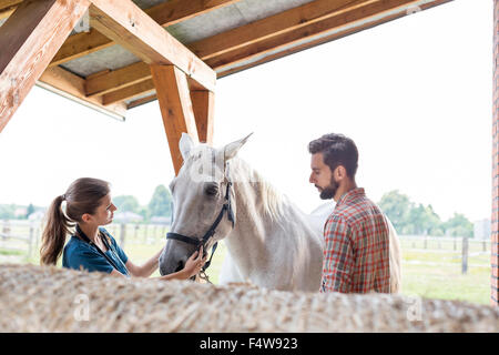 Couple petting horse in rural stable Stock Photo