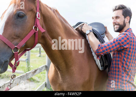 Smiling man removing saddle from horse Stock Photo