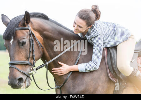 Smiling woman horseback riding leaning and petting horse Stock Photo