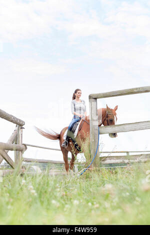 Woman horseback riding in fenced rural pasture Stock Photo