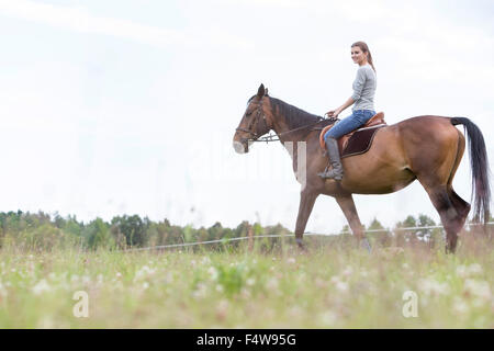 Woman horseback riding in rural field Stock Photo