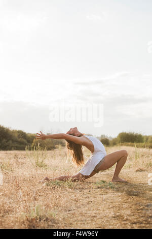 Boho woman in high crescent lunge yoga pose in sunny rural field Stock Photo