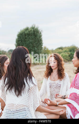 Boho women meditating in circle in rural field Stock Photo