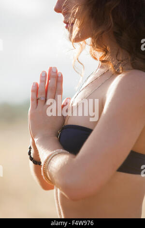 Close up serene woman in bikini meditating with hands at heart center Stock Photo