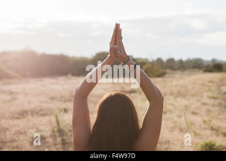 Woman meditating with hands clasped overhead in sunny rural field Stock Photo