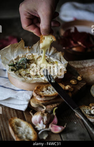 Someone take a piece of Baked Coulommiers cheese Stock Photo