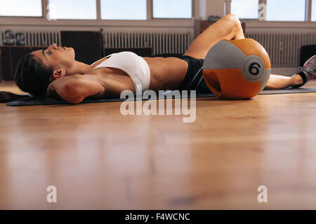 Image of young woman relaxing on exercise mat after intense workout at gym. Fit female athlete lying on floor. Stock Photo