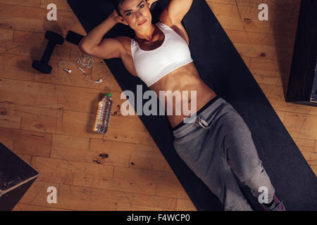 Overhead shot of fit young woman lying on yoga mat with her hands behind head and looking at camera. Determined female ready to Stock Photo