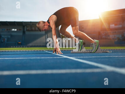 Young man on starting position ready for running. Male athlete in the starting blocks on sports track about to run. Stock Photo