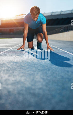 Professional male track athlete in set position on sprinting blocks of an athletics running track in stadium. Stock Photo