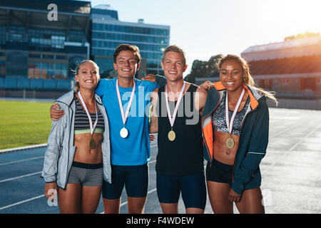 Group of athletes with medals .Two young woman and man together looking at camera and smiling while standing on athletics race t Stock Photo