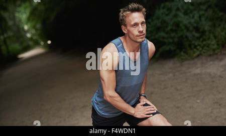 Athletic handsome man warming up before his workout or jog doing stretching exercises outdoors on a track in a wooded park Stock Photo