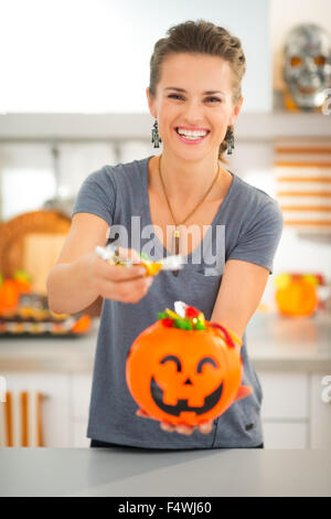 Сandy will suffice for all! Young smiling woman holding halloween Jack-o-Lantern bucket and giving trick or treat candy. Traditional autumn holiday Stock Photo