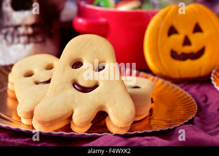 closeup of a golden tray with some ghost-shaped cookies and a pumpkin-shaped cookie, a bowl with halloween candies and a scary s Stock Photo