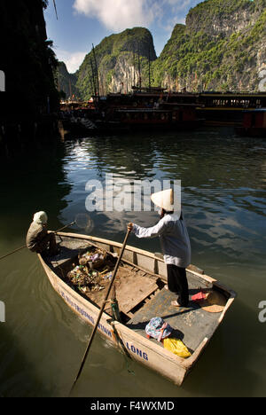 Woman rowing a boat, collecting rubbish from tourist boats, Halong Bay, Viet Nam. Rowing a boat through Halong Bay, Vietnam. Cat Ba harbour Halong Bay Gulf of Tonkin Vietnam South East Asia. Stock Photo