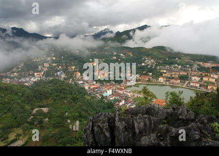 Sapa Village. Aerial view of clusters of buildings nestled in the green valley of Sapa, Vietnam. View over Sapa town with clouds rolling in through mountains Vietnam. Stock Photo