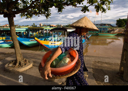 Traditional boats on the Song Thu Bon river, Hoi An, Vietnam, Southeast Asia. Woman with a traditional hat passing in front of the pier. Stock Photo