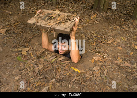 Tourist gliding into the entrance of the Viet Cong tunnel system in Cu Chi, Vietnam, Asia. Tourist with arms above head demonstrates how to enter the Cu Chi Tunnels Vietnam. Stock Photo