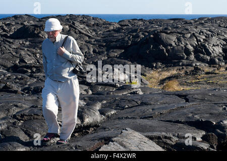 Tourist walking over the Black lava mountains near the coast and highway Chain of Crater Road. Hawai'i Volcanoes National Park. Stock Photo