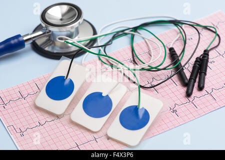 Electrocardiogram leads and electrocardiograph and stethoscope on blue table. Stock Photo