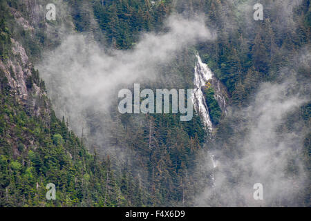 A scenic mountainside waterfall crashes down the cliff face through the clouds near Skagway Alaska | Lynn Canal fjord cruise - inside passage Stock Photo