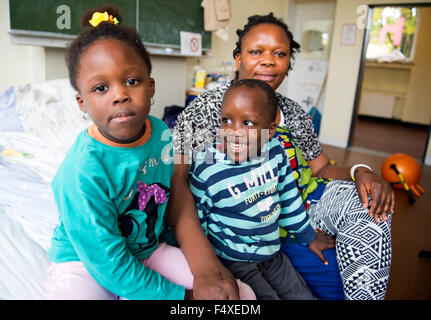 Duesseldorf, Germany. 22nd Oct, 2015. Evbuomwan Zoreth from Nigeria sits with her children Silvia (6) and David (5) on a bed in a refugee shelter in Duesseldorf, Germany, 22 October 2015. Photo: Monika Skolimowska/dpa/Alamy Live News Stock Photo