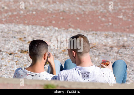 Two men sitting on the steps drinking beer on Oddicombe Beach looking out to sea on hot day in Torquay, Devon, England Stock Photo