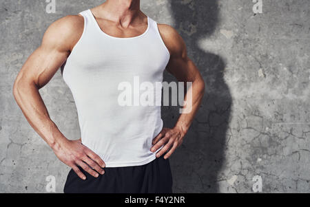 Close up fitness portrait of white muscular man in white tank top, standing on grey background, copy space, fitness concept Stock Photo