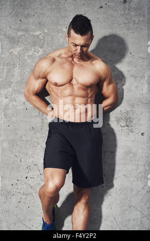 Muscular fit and healthy man standing on grey background, looking down, wearing no shirt and black shorts. Fitness concept abdom Stock Photo