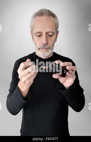 A mature man is pouring cough syrup in a spoon to cure his sore throat and bronchitis Stock Photo