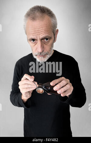 A mature man is pouring cough syrup in a spoon to cure his sore throat and bronchitis Stock Photo