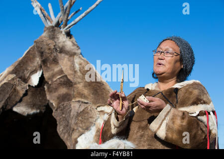 Canada, Nunavut, Hudson Bay, Kivalliq, Arviat, local woman demonstrates historic tools used by Inuit, polar tent in background. Stock Photo