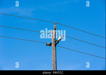 Old simple rural weathered wooden utility pole with three parallel cables and insulators against blue sky. Stock Photo