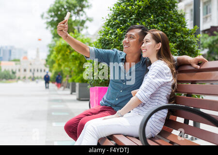 Asian couple taking selfie portrait picture sitting bench Stock Photo