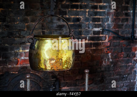 Single Antique vintage 1590 cauldron hand forged cooking pot hangged by the hearth fireplace old golden Stock Photo