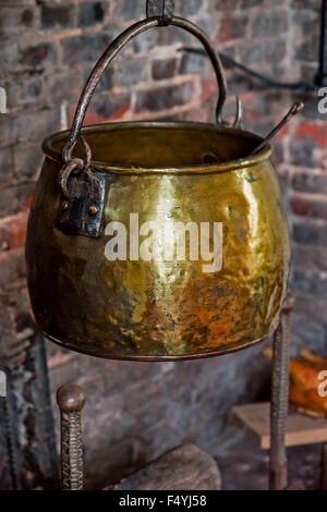 Single Antique vintage 1590 cauldron hand forged cooking pot hangged by the hearth fireplace old golden Stock Photo
