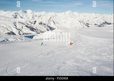 View down a piste with skiers and mountains Stock Photo