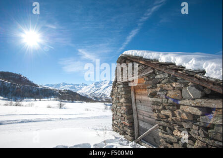 Remote alpine mountain hut on a slope in the sunlight covered with snow Stock Photo