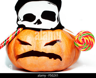 halloween holiday traditional scary smiling orange pumpkin in black skull hat and candys isolated on white background Stock Photo