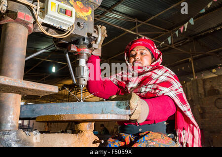 Woman drilling a hole in a metal bar, working at a drilling machine Stock Photo