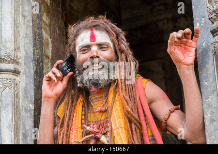 Sadhu, Holy Man, using his mobile phone opposite the burning ghats near Pashupatinath Temple Stock Photo