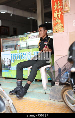 Police man with automatic rifle and mobile phone guarding money exchange in Sisophon, Cambodia Stock Photo