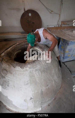 Baker placing dough into a clay oven in Tbilisi, Georgia Stock Photo