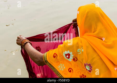 Woman in yellow sari washing cloths at the Sangam, the confluence of the rivers Ganges, Yamuna and Saraswati, at Kumbha Mela Stock Photo