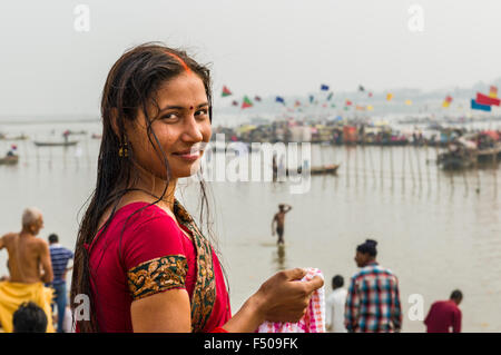 Young woman in red sari smiling at the Sangam, the confluence of the rivers Ganges, Yamuna and Saraswati, at Kumbha Mela, many b Stock Photo