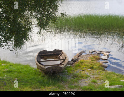 Old wooden rowing boat on the shore of small Norwegian lake, weathered, worn, waterlogged and in need of repair