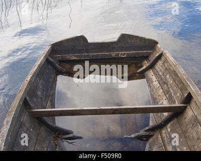 Old wooden rowing boat on the shore of small Norwegian lake, weathered, worn waterlogged and in need of repair, sky reflections