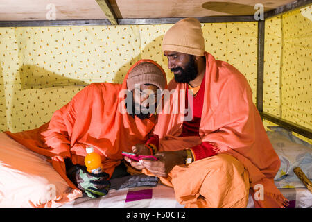 Two Sadhus, holy men, are playing with a smartphone in a tent Stock Photo