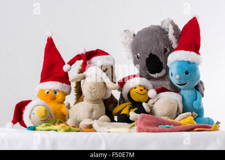 Many colorful cuddly toys, wearing Santa Claus hats, are sitting together on a white table Stock Photo